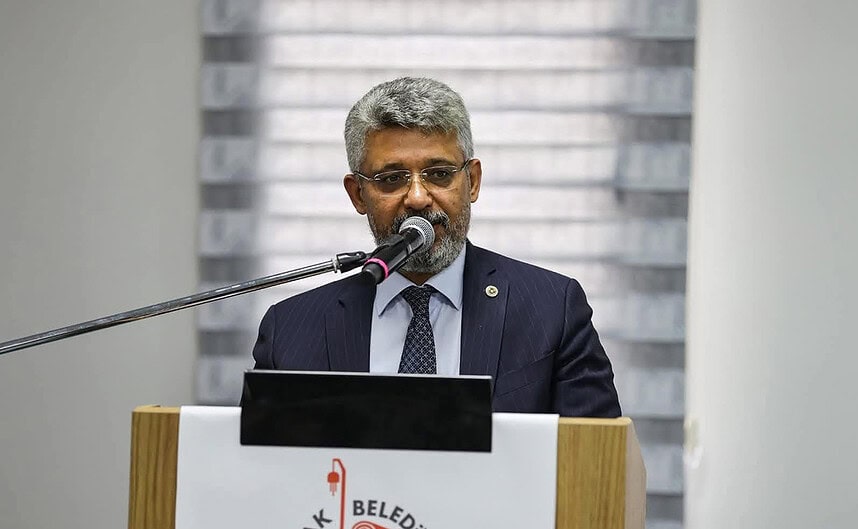 Nüfus müdürü, belediye toplantısında konuşma yaparken mikrofon kullanıyor.