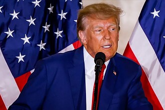 Donald Trump, Kanada'ya yönelik sert açıklamalar yaparken, Amerikan bayrakları önünde konuşuyor.