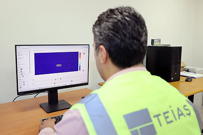 Çalışan, bilgisayar başında tehlike uyarı yeleğiyle bakanlık logosuyla, ofis ortamında teknik analiz yapıyor.