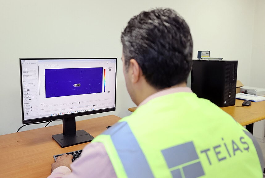 Çalışan, bilgisayar başında tehlike uyarı yeleğiyle bakanlık logosuyla, ofis ortamında teknik analiz yapıyor.