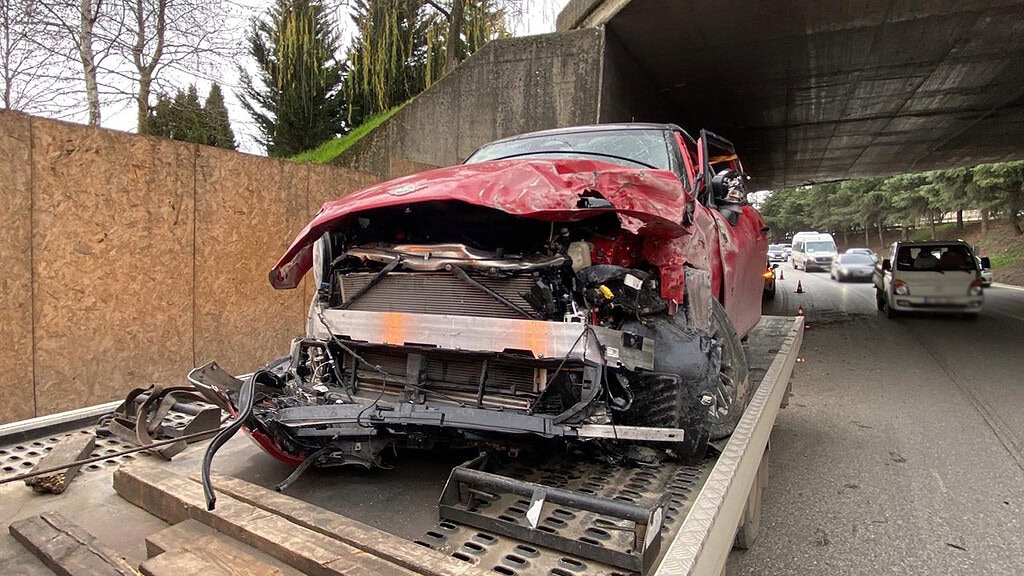 Kaza sonrası ciddi hasar almış kırmızı araba, olay yerinde yıkılmış ve yaklaşık olarak hasarlı halde duruyor.