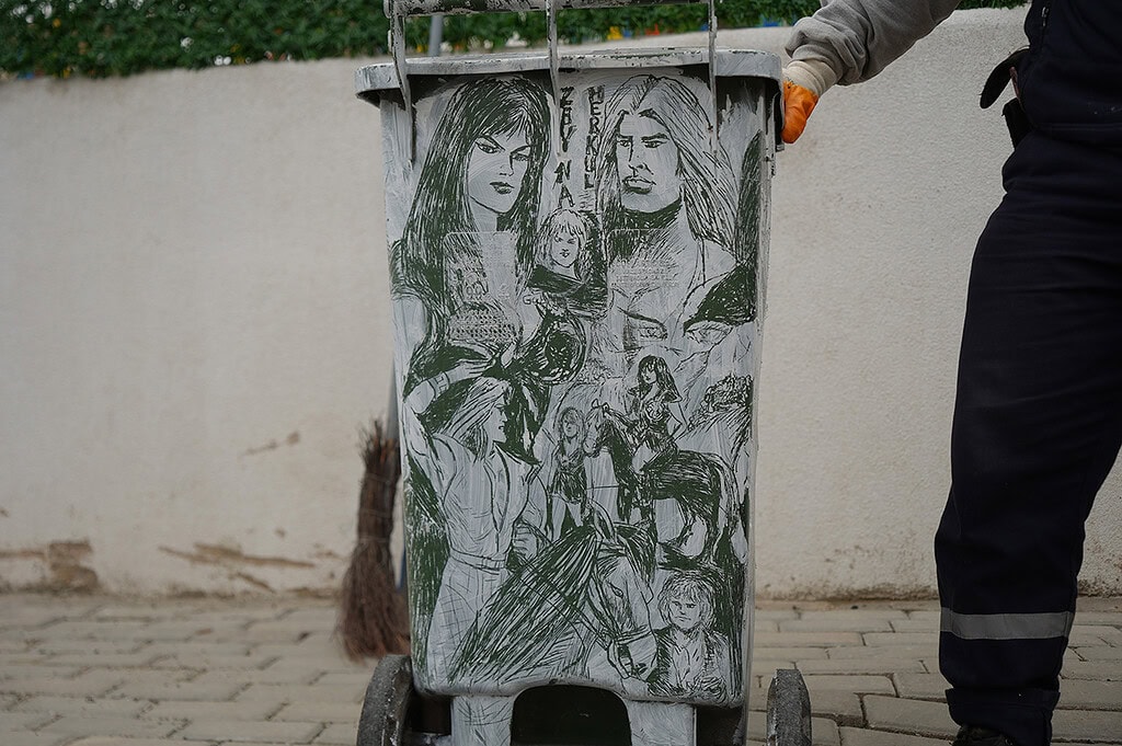 Çöp kutusuna çizilmiş kadın ve çocuk figürleriyle sanat eseri.
