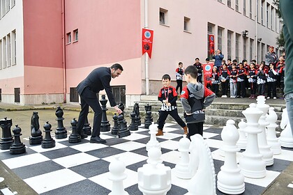 Başkan Yasin Özlü, şampiyon kız takımıyla satranç oynarken, büyük ilgiyle izleyen kalabalık ve çocuk.